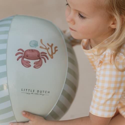 Bola listrada verde clara e branca com caranguejo e texto Little Dutch, segurada por criança com camisa xadrez amarela.