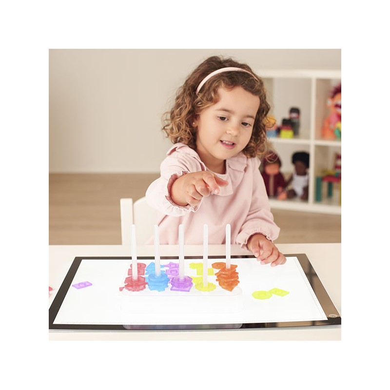 Menina a brincar com jogo educativo de formas coloridas em mesa branca