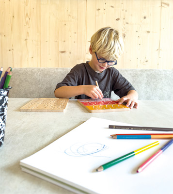 Criança a desenhar numa mesa com lápis de cor e caderno