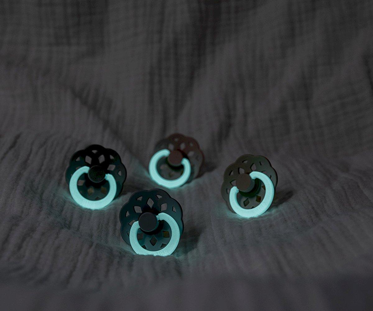 Quatro chupetas de bebê com anel luminoso azul claro e parte superior escura perfurada em tecido cinzento