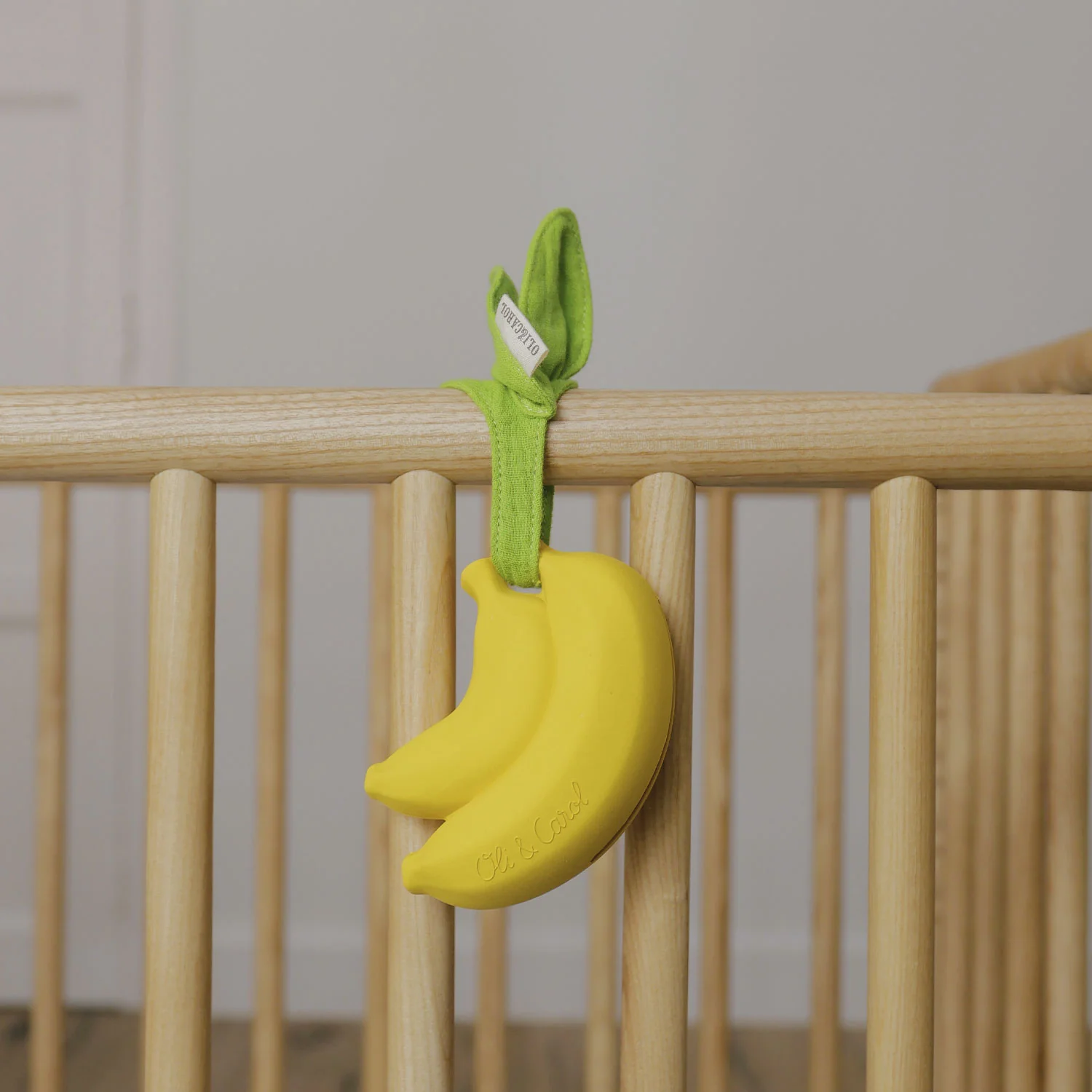Brinquedo em forma de cacho de banana amarelo pendurado em berço de madeira clara