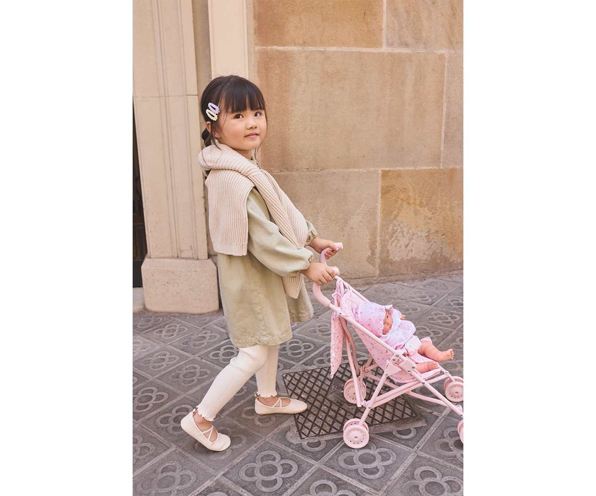 Menina a empurrar carrinho de bonecas rosa na rua