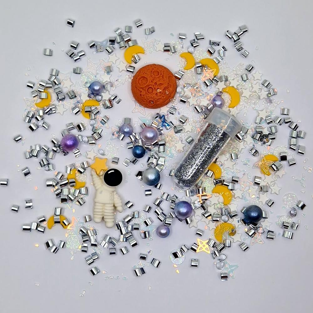 Confetes coloridos variados com astronauta miniatura e frasco com glitter prateado sobre superfície branca