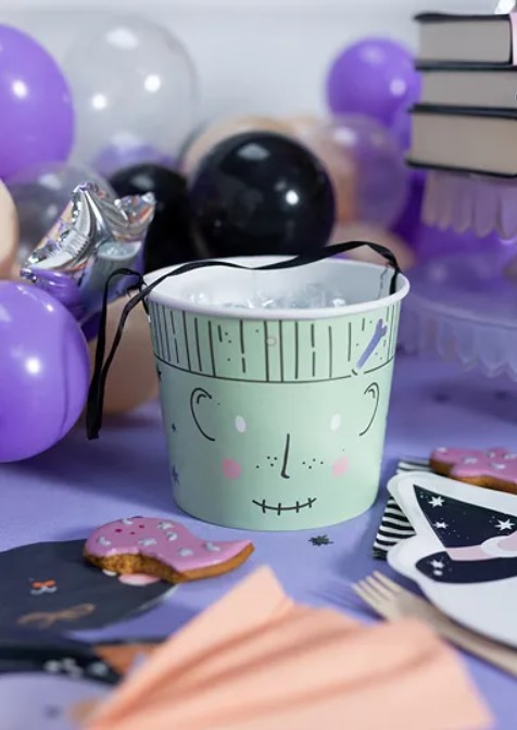 Balde de papel verde com rosto desenhado, rodeado de balões e artigos de festa