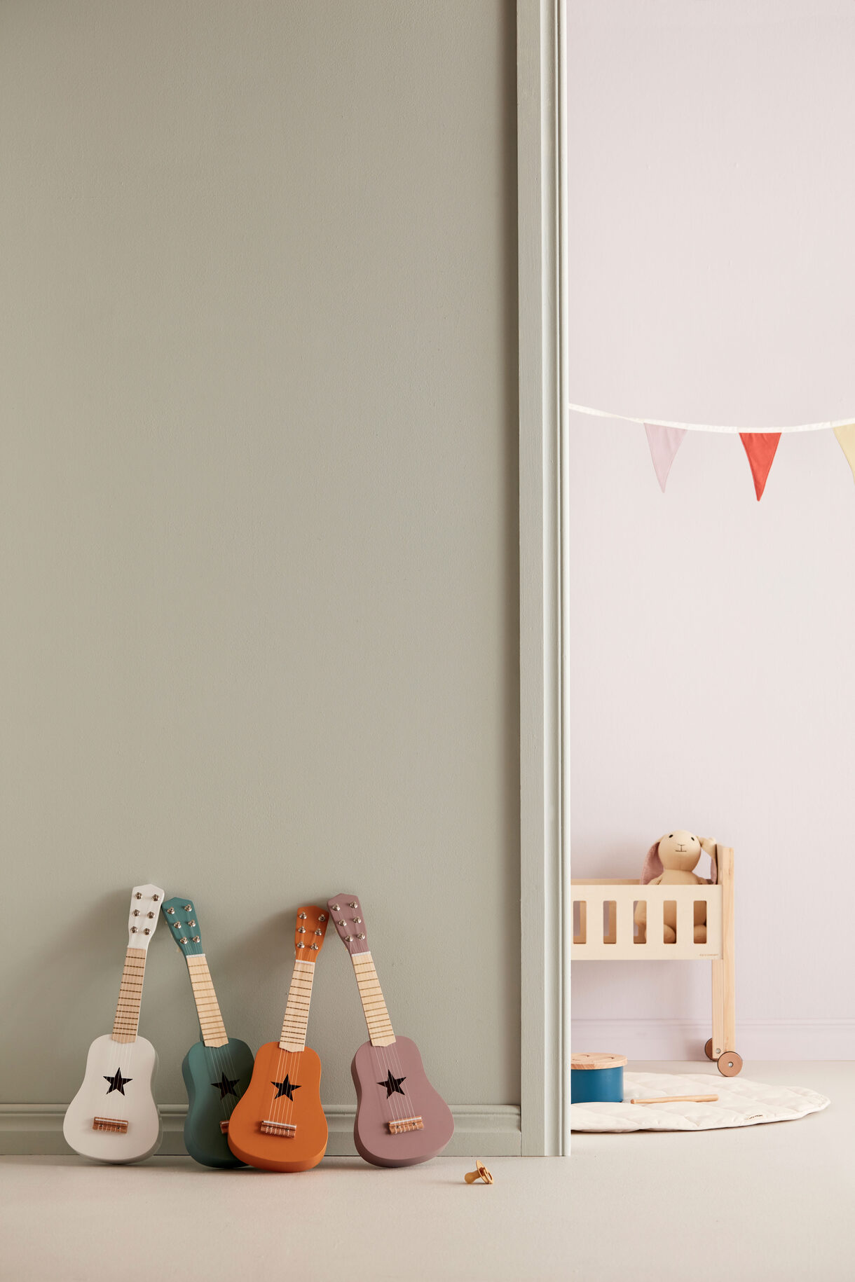 Quatro guitarras de brinquedo em madeira com cama de bebé e boneco de peluche ao fundo