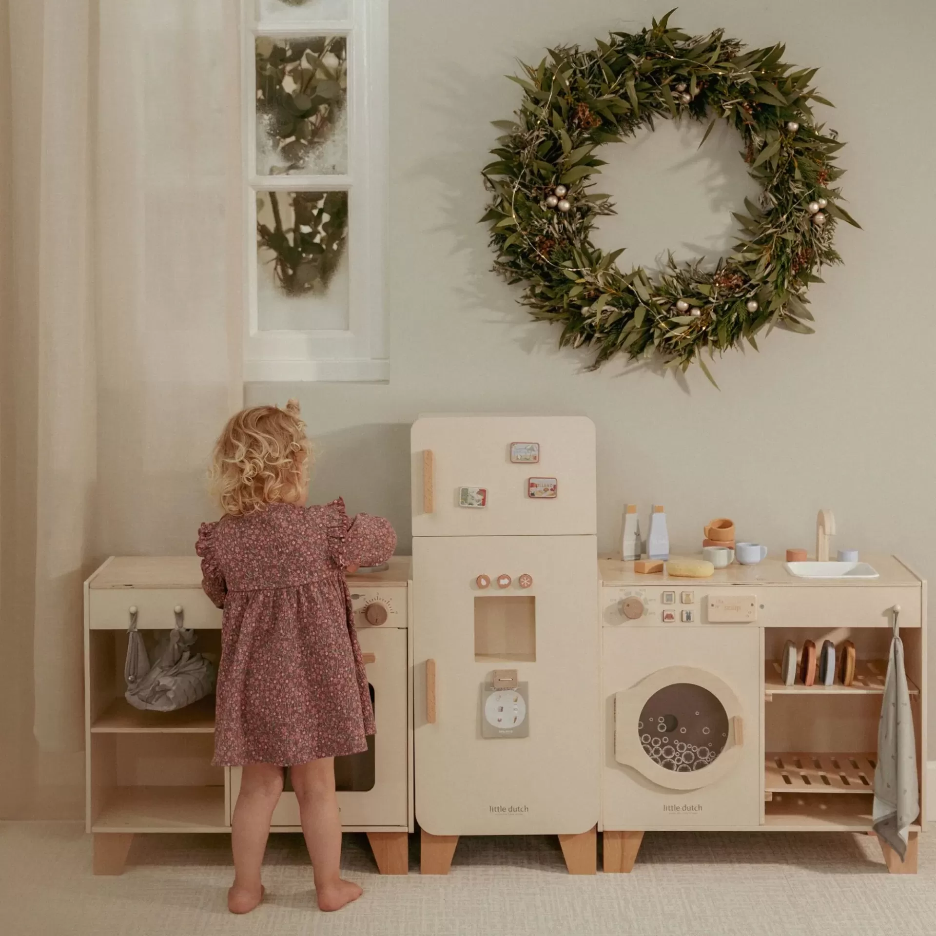 Cozinha de brincar em madeira clara com acessórios e criança de vestido rosa
