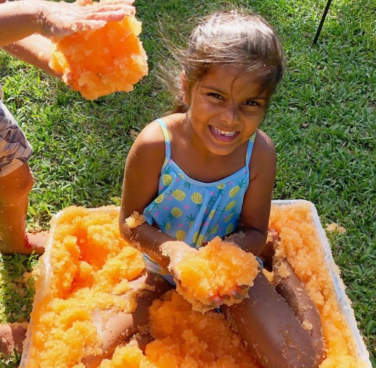 Criança a brincar com gelo colorido num recipiente amarelo ao ar livre