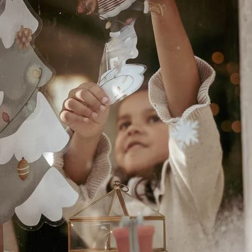 Menina a decorar árvore de Natal com ornamento branco e transparente