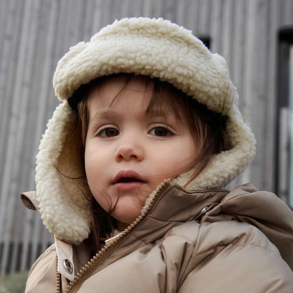 Criança com casaco bege acolchoado e chapéu forrado de lã sintética