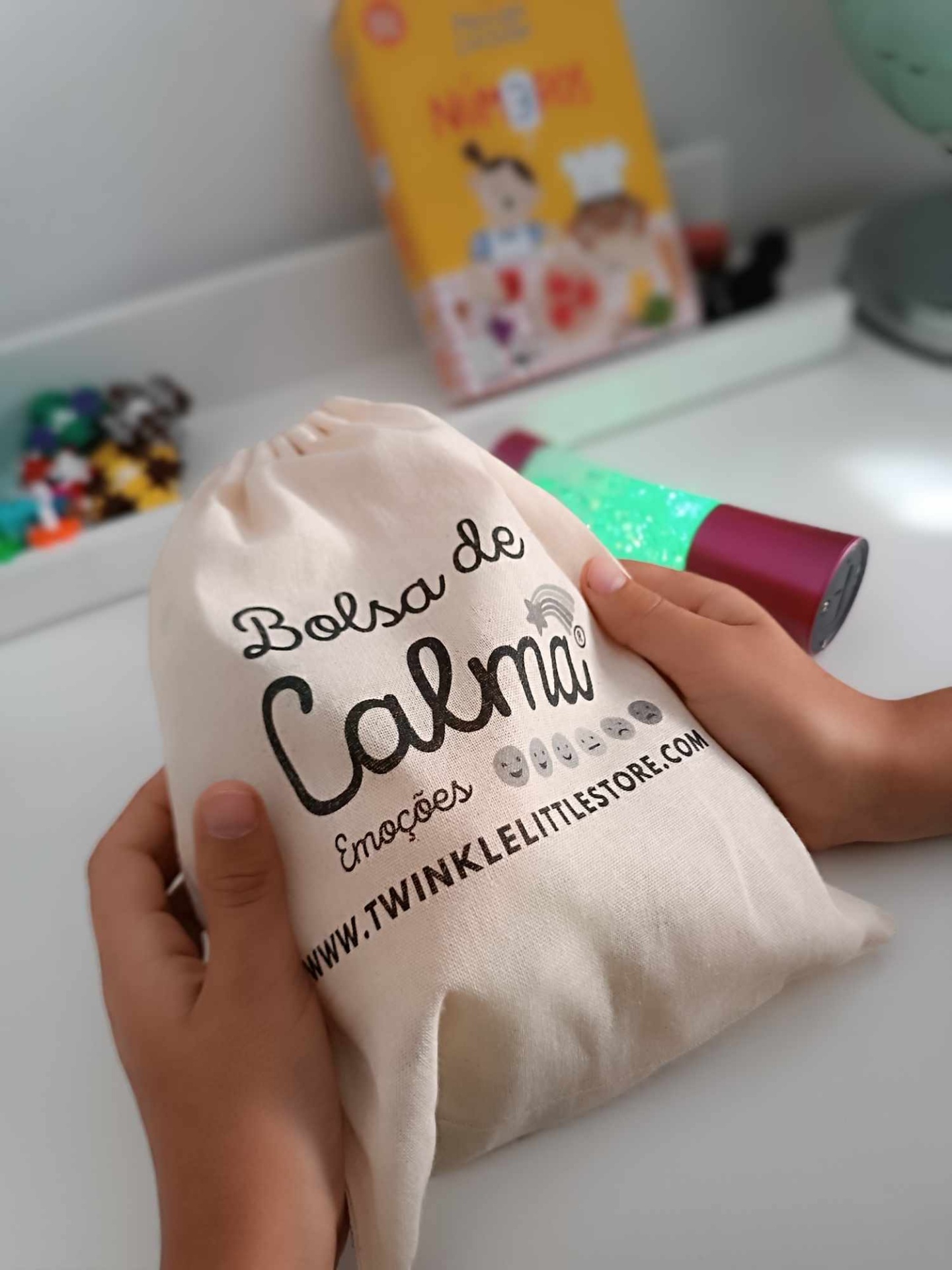 Bolsa de tecido creme com texto em preto segurada por mãos sobre mesa branca
