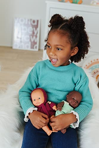 Menina com camisola verde sentada a segurar duas bonecas