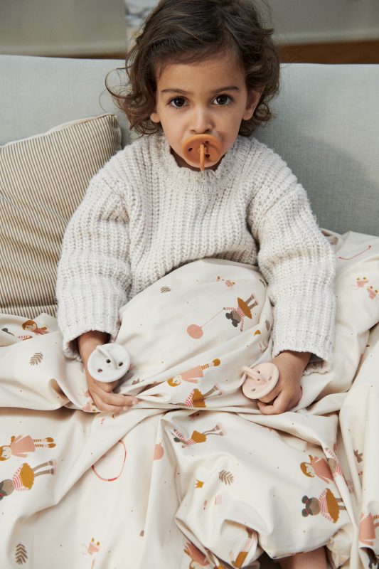 Criança com chupetas de silicone e edredão estampado sentada no sofá