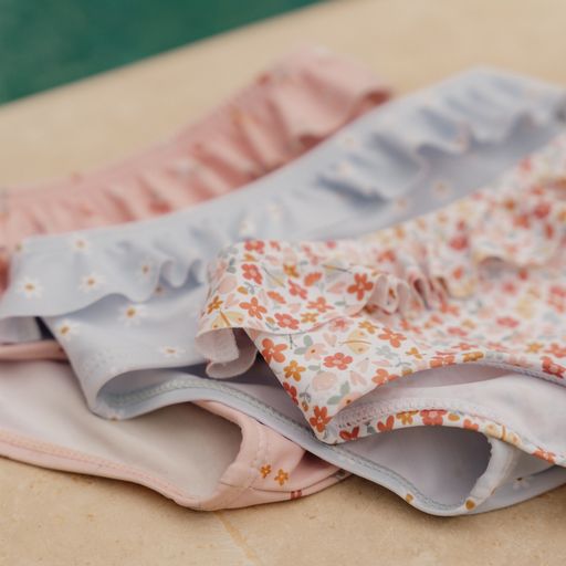 Três cuecas de criança em algodão com padrões florais e folhos, sobre uma superfície de mármore