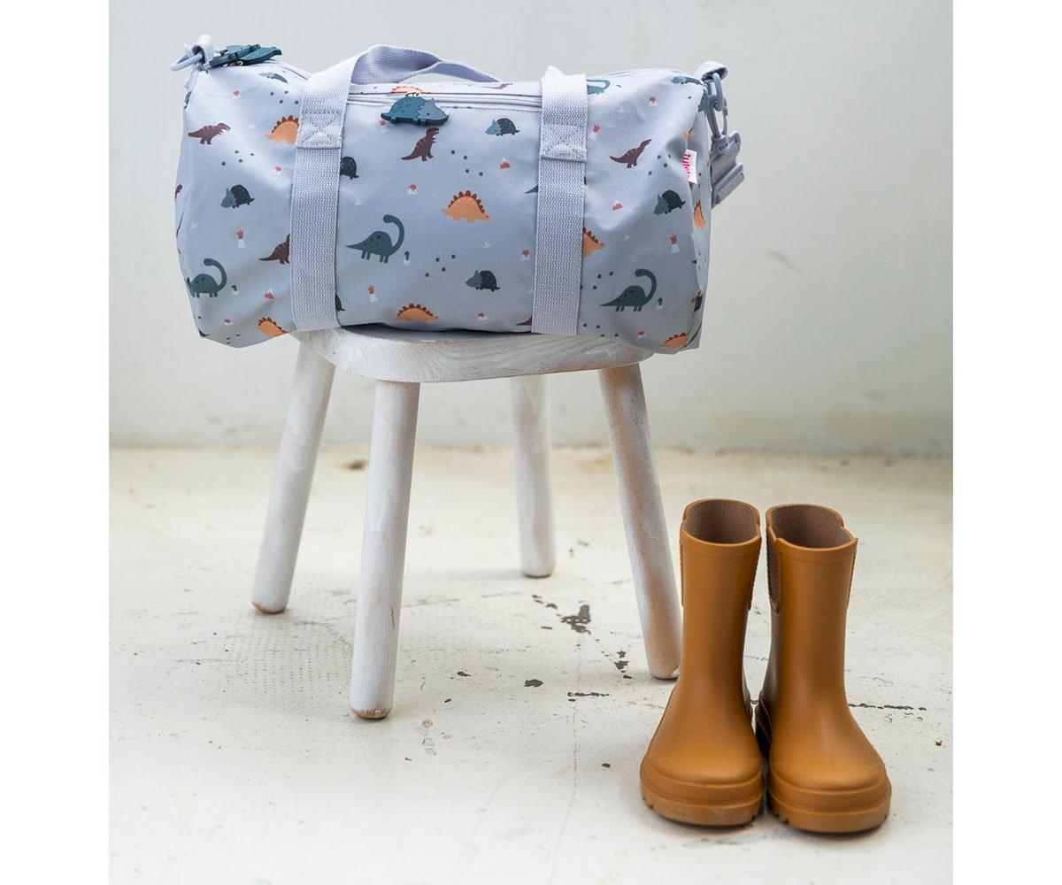 Mala azul claro com padrão de dinossauros e botas castanhas claras ao lado