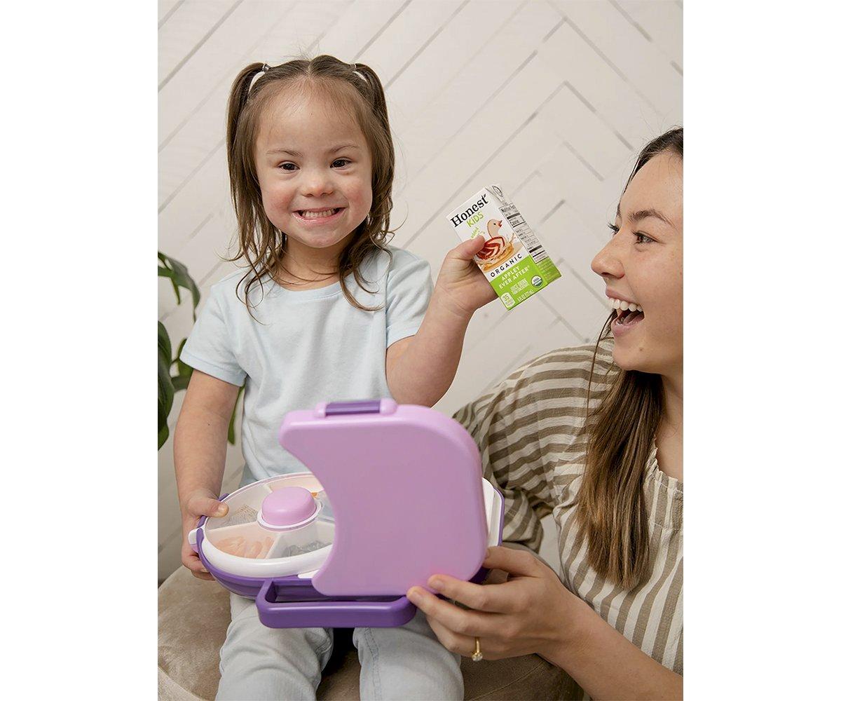 Criança sorridente com caixa de sumo, mulher ao lado, brinquedo lilás