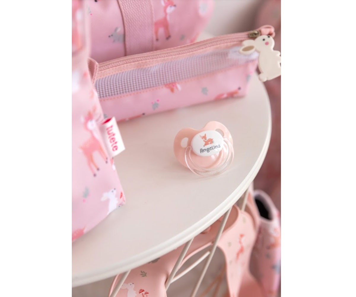 Chupeta rosa transparente ao lado de bolsa rosa com padrão de cervos e flores.