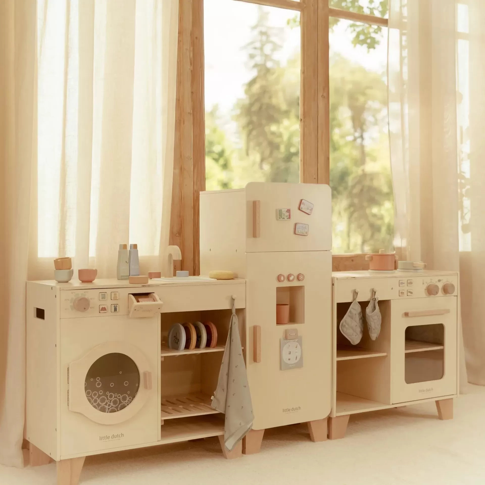 Cozinha de madeira creme para crianças com máquina de lavar, frigorífico e forno, acessórios e cortinas claras ao fundo