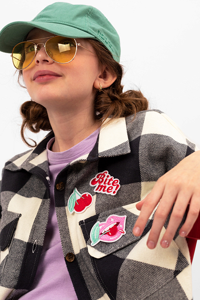 Casaco xadrez preto e branco com patches e mulher a usar boné verde e óculos de sol amarelos