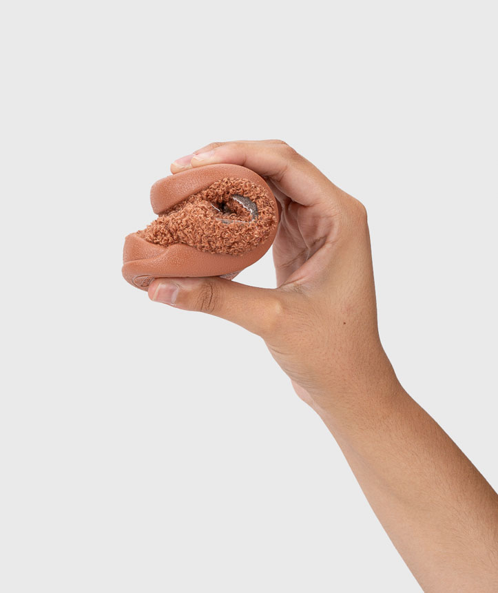 Mão segurando sapato castanho flexível com interior felpudo