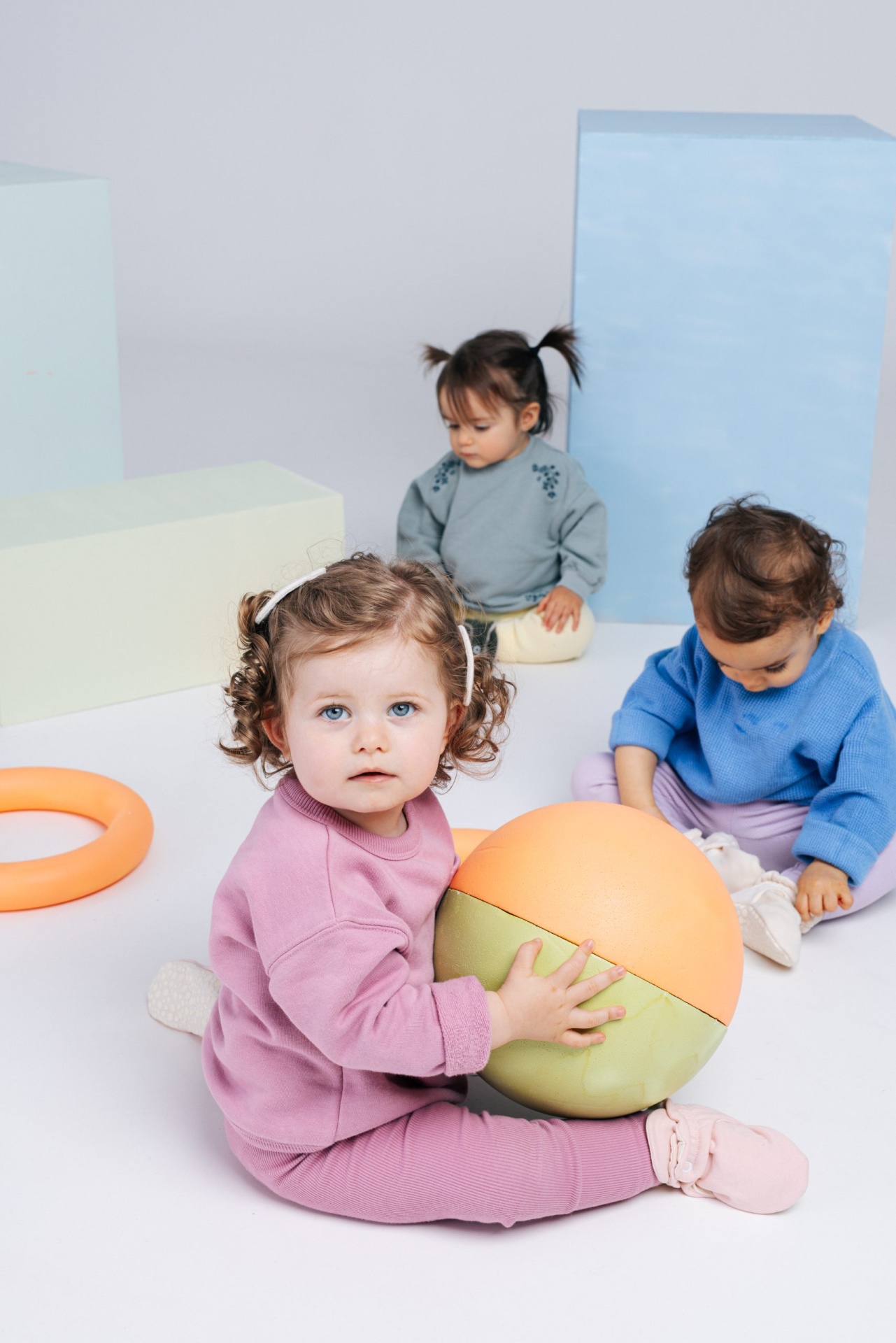 Três bebés sentados com roupa colorida em estúdio branco e blocos coloridos