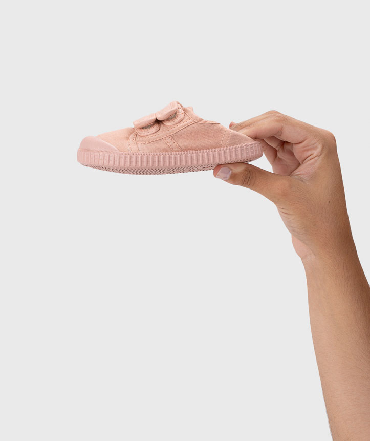 Sapato infantil cor de rosa com velcro sendo segurado por uma mão