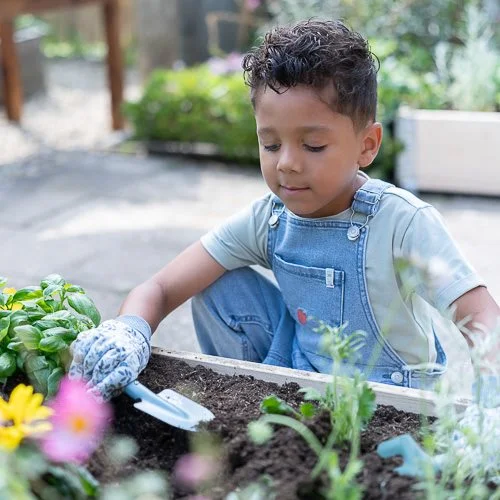 Criança com macacão a fazer jardinagem numa cama de plantação ao ar livre