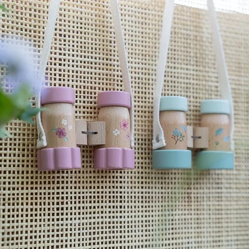 Quatro binóculos infantis de madeira com extremidades rosa e azul pendurados numa tela de malha bege