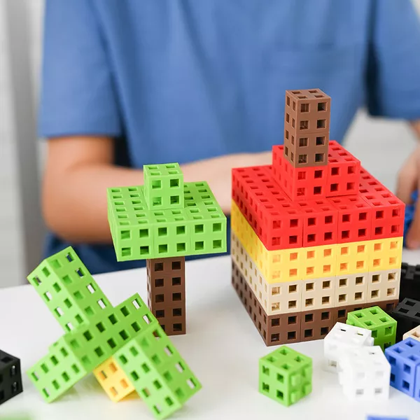 Blocos de construção coloridos em formas de casa e árvores, com uma pessoa ao fundo