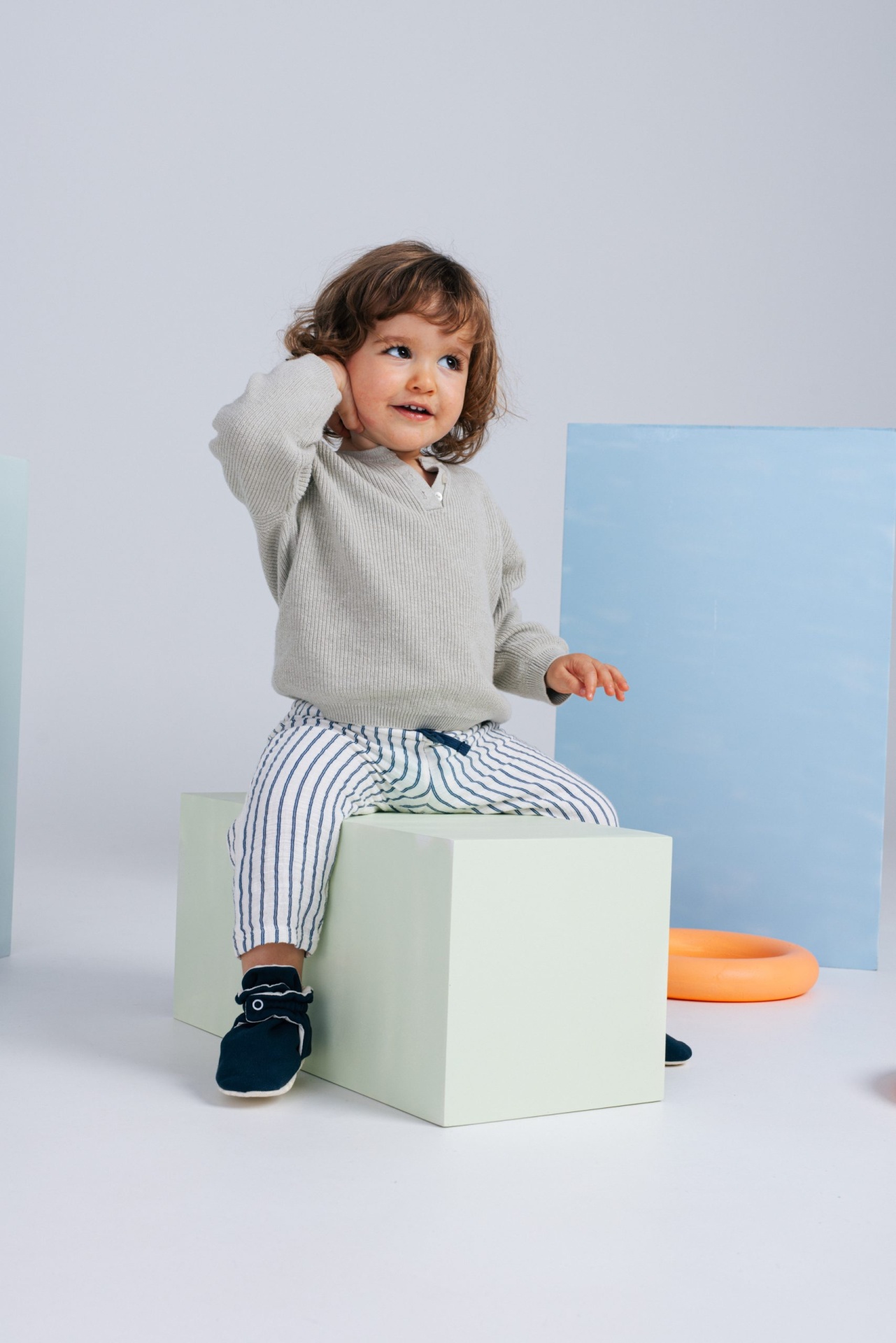 Criança sentada com camisola cinzenta, calças às riscas e sapatos azuis