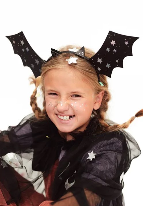 Menina com fantasia preta de morcego e tiara com asas decoradas com estrelas