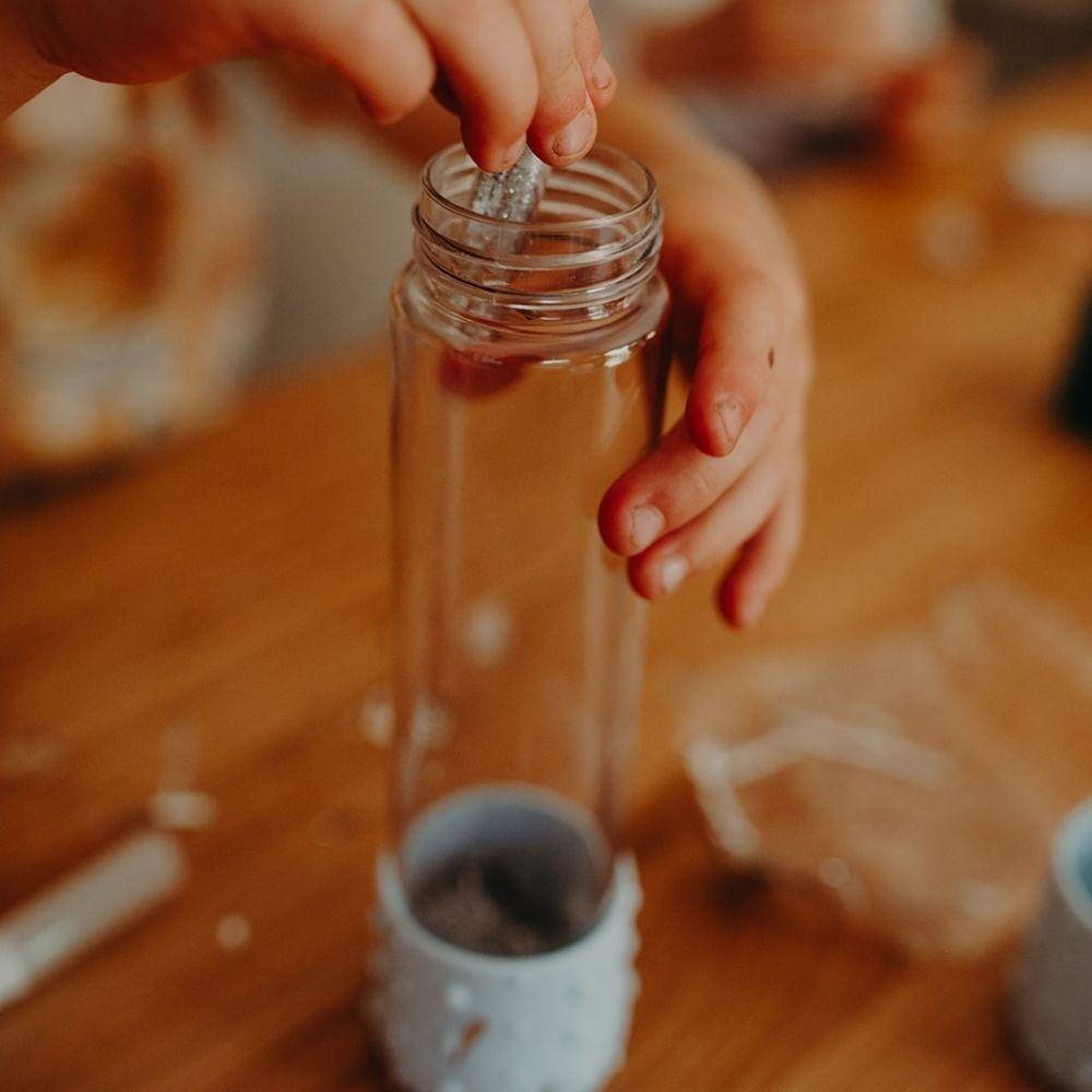 Garrafa de vidro com base texturizada azul clara e mão inserindo objeto transparente