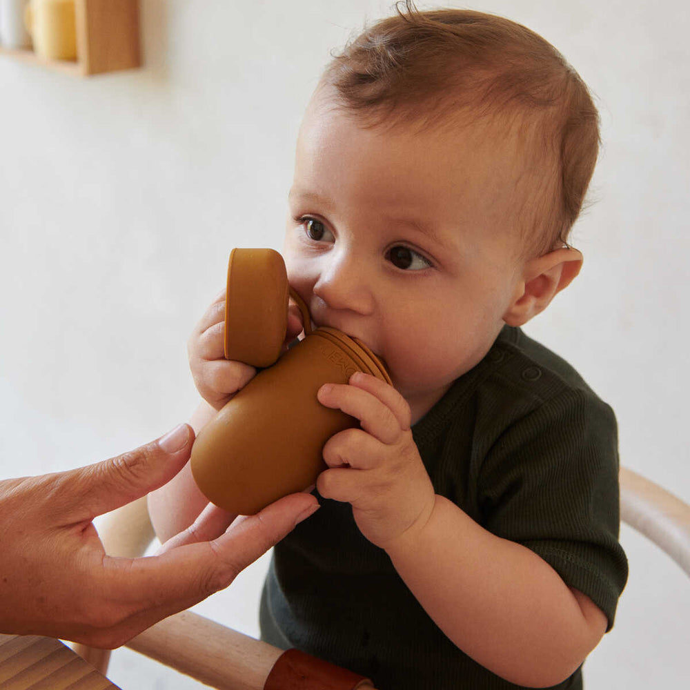 Criança com recipiente de silicone marrom numa cadeira alta