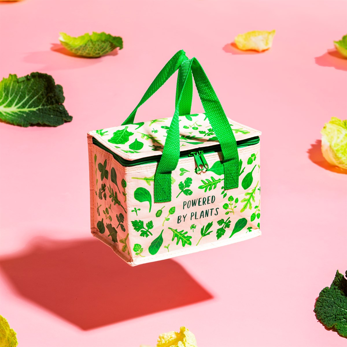 Saco térmico creme com desenhos verdes e alças verdes sobre fundo rosa com folhas