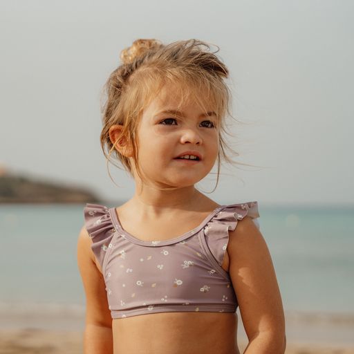 Criança na praia com top de biquíni lilás com flores brancas e folhos