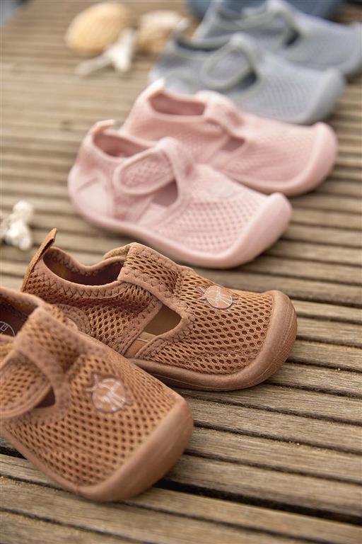 Três pares de sapatos infantis em malha castanho, rosa e azul claro sobre piso de madeira