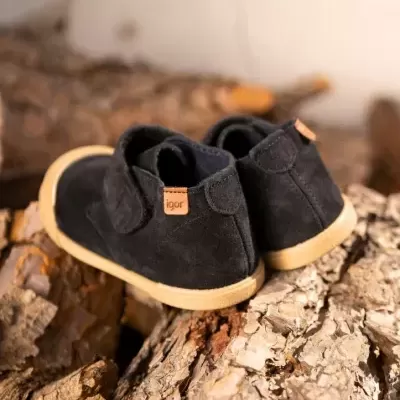 Sapatilhas pretas de criança com sola bege e etiqueta 'igor' sobre troncos de árvore.