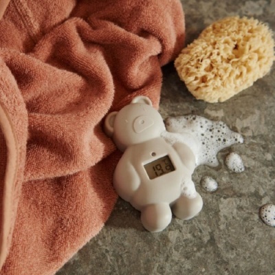 Termómetro digital em forma de ursinho branco junto a toalha ferrugem e esponja natural