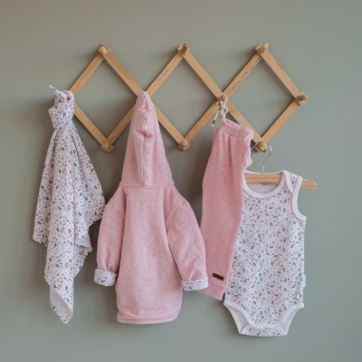 Conjunto de roupa infantil rosa e branco com padrão floral suspenso em cabideiro de madeira