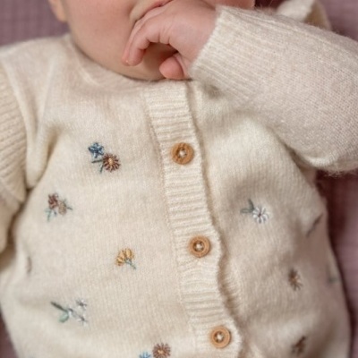 Criança com casaco de malha creme com bordados florais e botões de madeira.