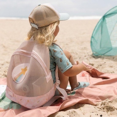 Criança com mochila rosa sentada na praia perto de tenda verde