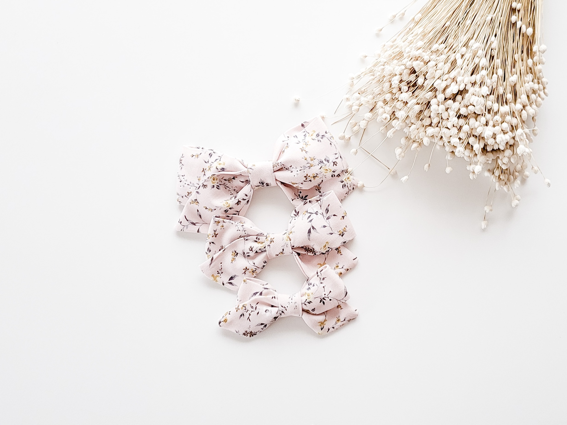 Três laços de tecido rosa com flores escuras e ramo de flores secas claras