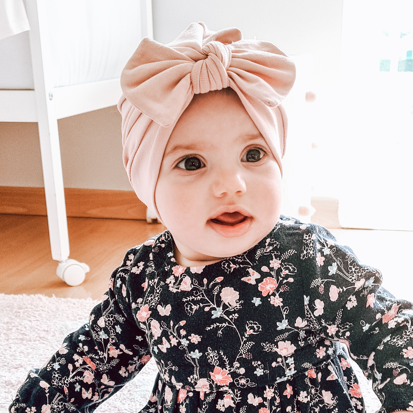 Bebé com turbante rosa e vestido floral sentado no chão