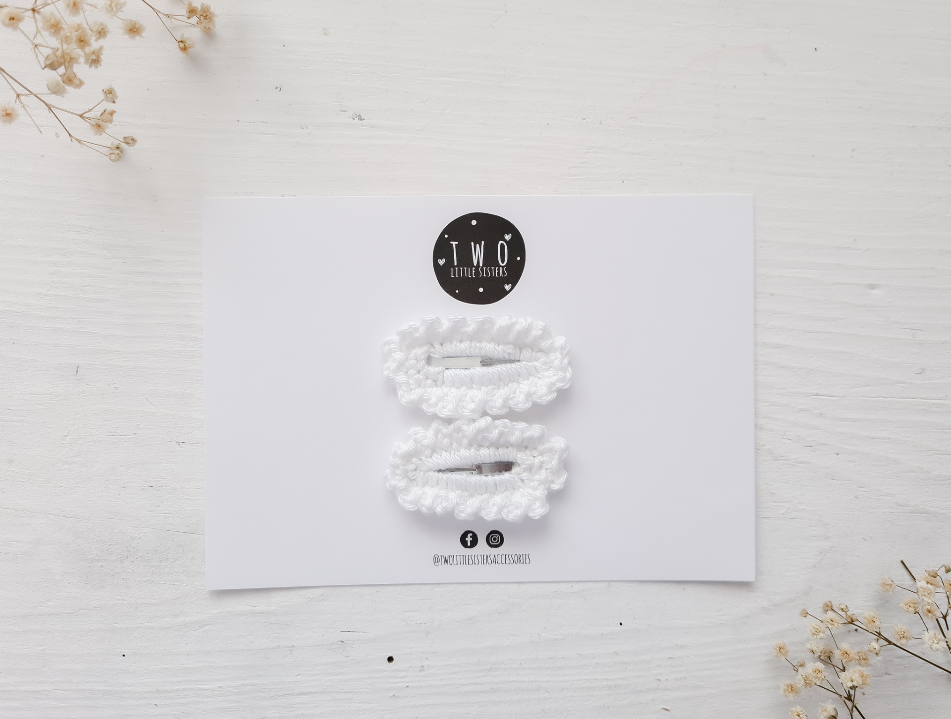 Ganchos de cabelo brancos em cartolina com marca TWO, sobre fundo branco com flores secas.