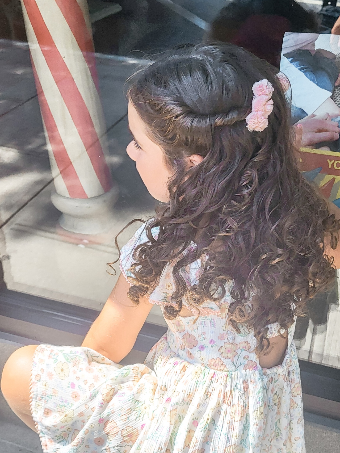 Menina com cabelo cacheado e vestido floral sentada junto a janela