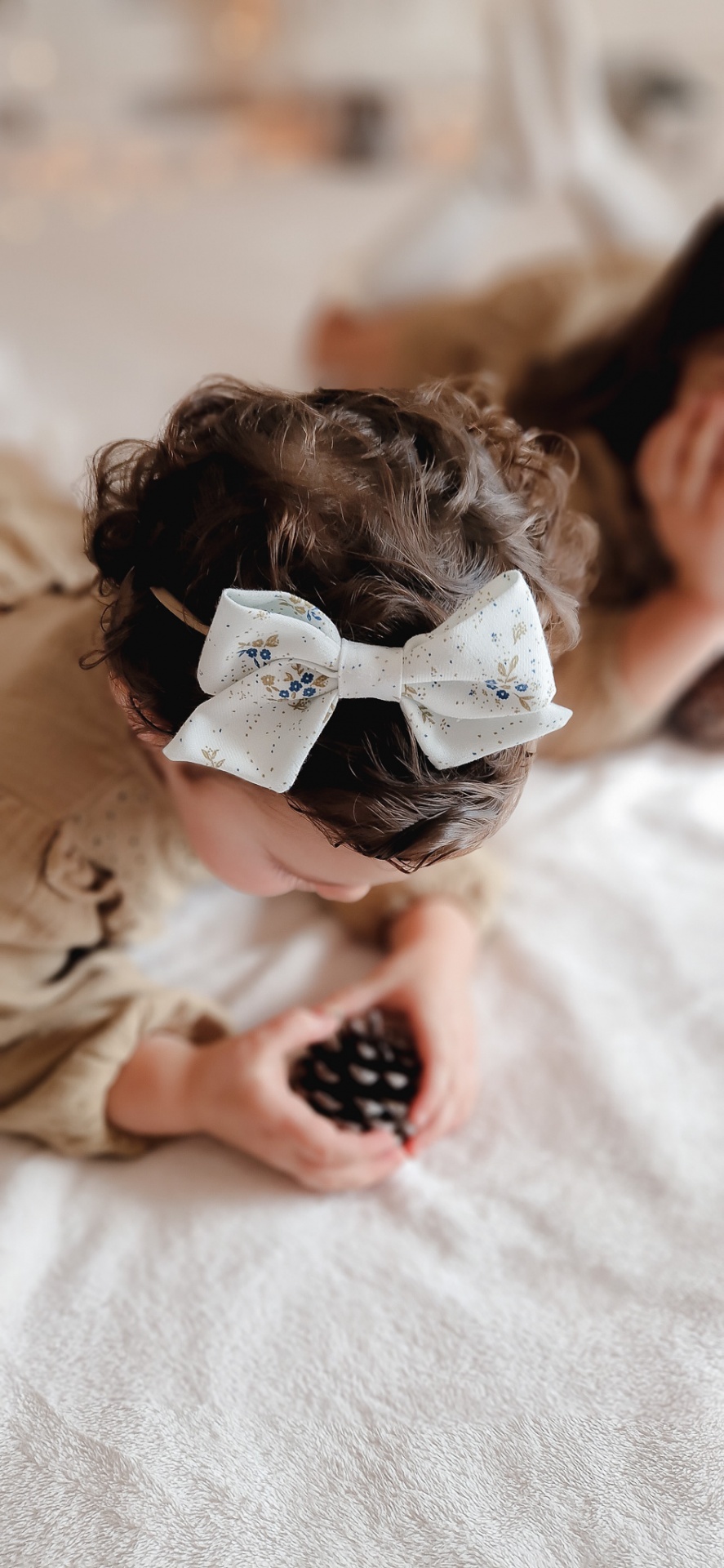 Laço branco com flores azuis e douradas no cabelo de criança encaracolada