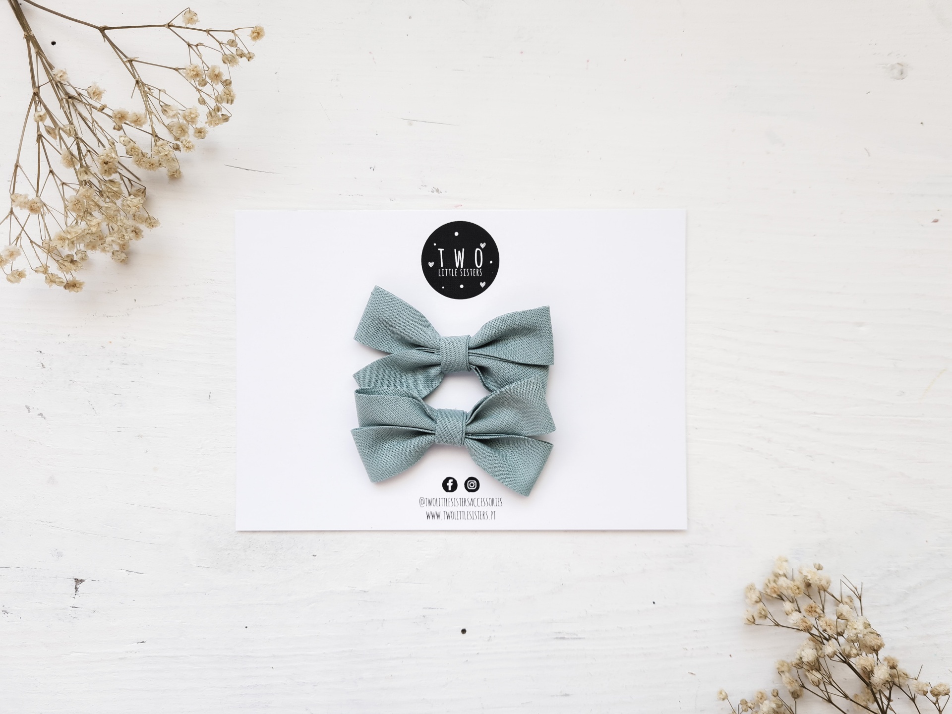 Dois laços azuis cinzentos em cartolina branca com logo TMØ design, raminhos de flores secas