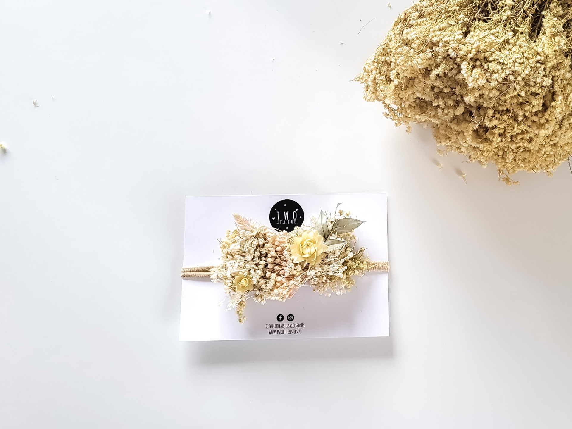 Fita decorativa creme e dourada com flores artificiais em cartão branco com logótipo e texto