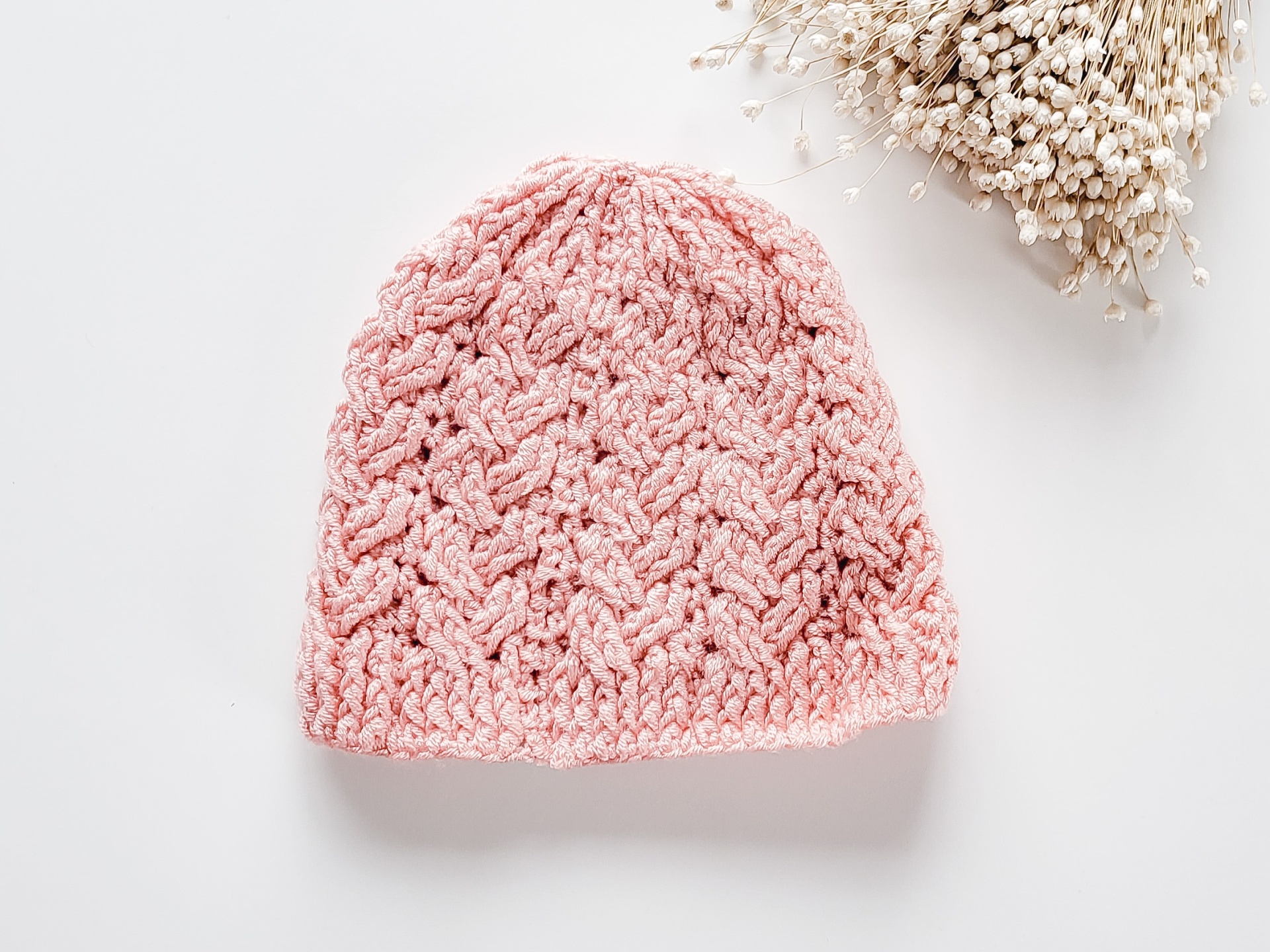 Touca cor-de-rosa tricotada com padrão em relevo e raminhos secos ao lado