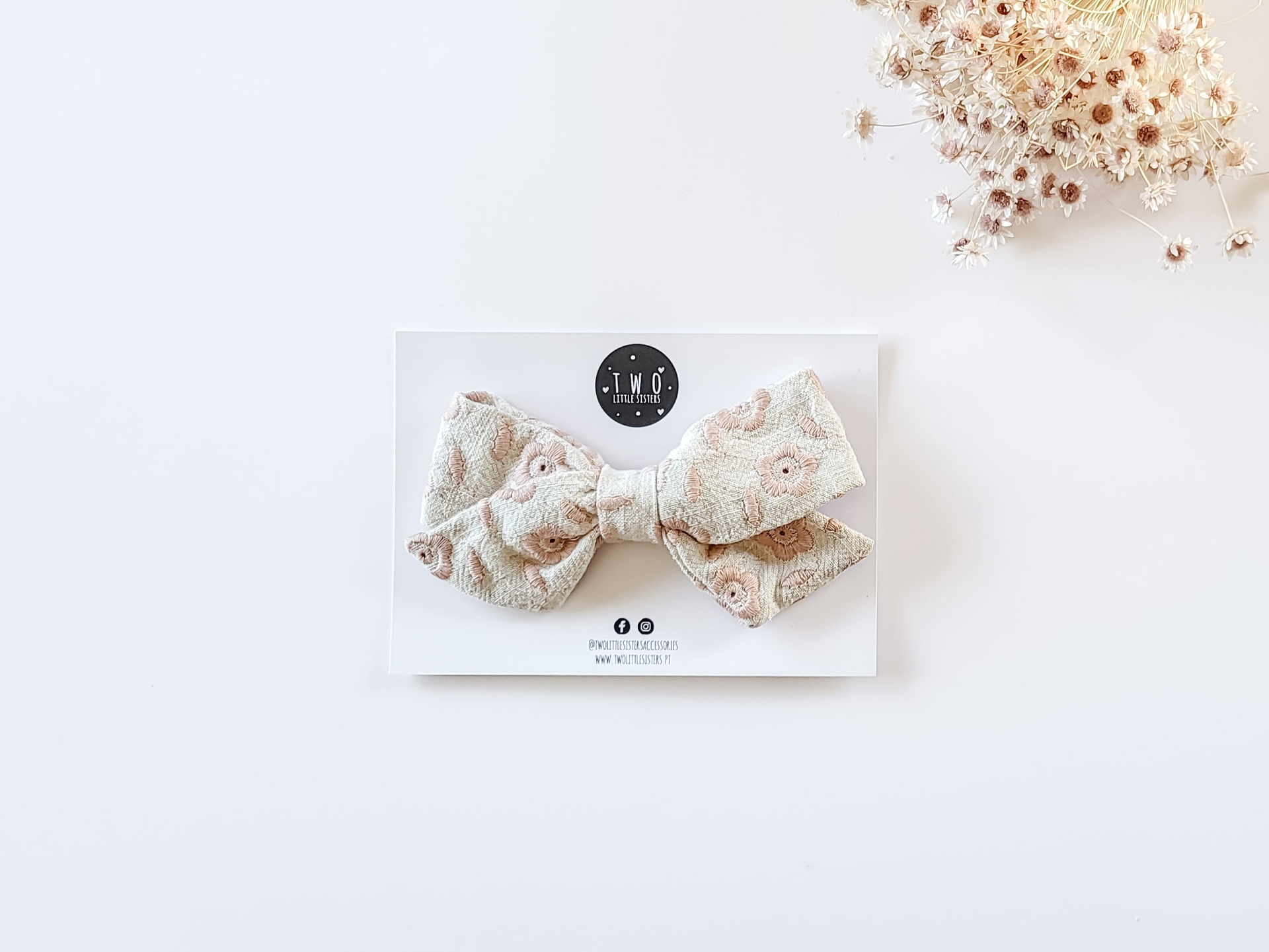 Laço de tecido bege com padrão floral rosa claro e branco preso num cartão branco