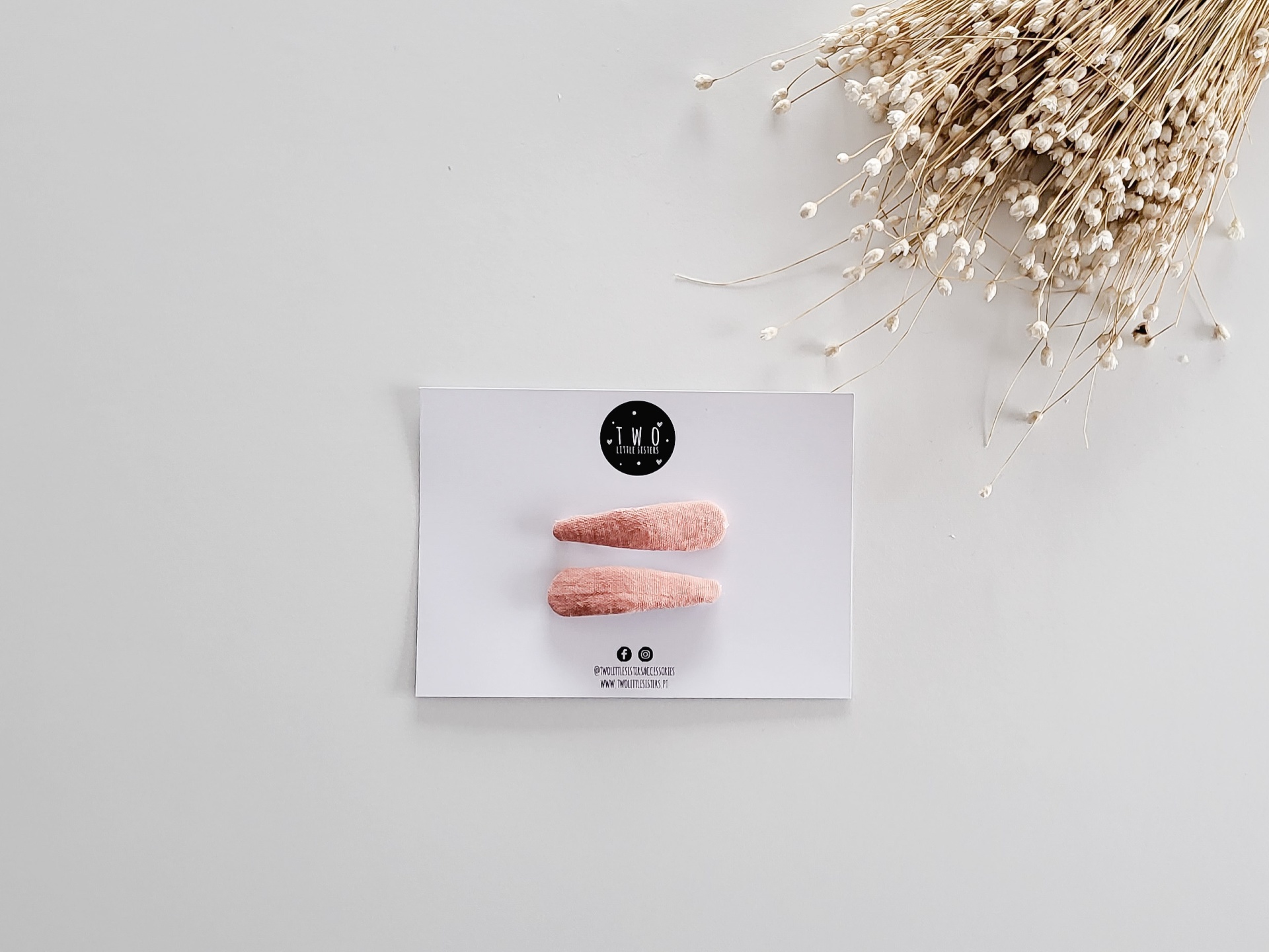 Molas de cabelo rosa claro em cartão branco com logótipo e plantas secas ao lado